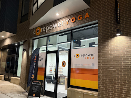 Nighttime exterior of CorePower Yoga Northern Liberties studio with orange and white signage, glass storefront, and "coming soon" banner.