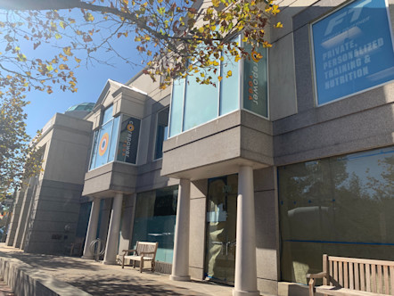 Modern gray building with large glass windows and columns touting the CorePower logo with a wooden bench in front