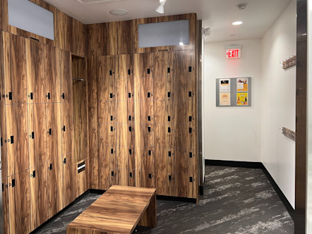 Combination of large and small wooden lockers with a matching wooden bench centered in front with patterned black and grey carpet