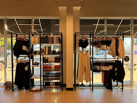 Modern clothing boutique with black metal racks displaying neutral-colored apparel and folded towels near large windows