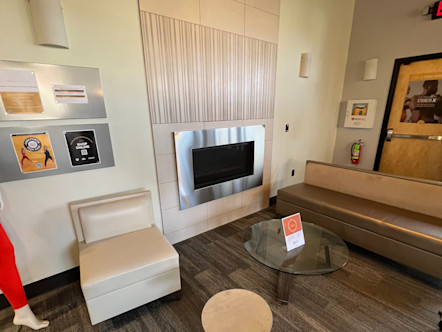 Encinitas studio lobby with a dark metallic couch and a cream chair around a glass table all in front of a light tan and metal fireplace