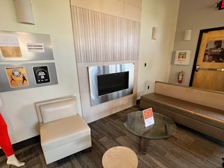 Encinitas studio lobby with a dark metallic couch and a cream chair around a glass table all in front of a light tan and metal fireplace