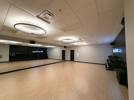 Empty CorePower Yoga studio with wooden floor, mirrored wall, circular ceiling lights, and weight equipment in the corner