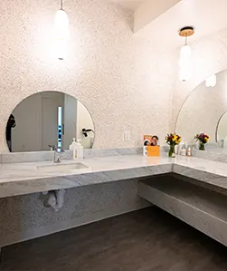 Modern bathroom vanity with round mirror, long countertop, sink, and flowers under pendant lights.