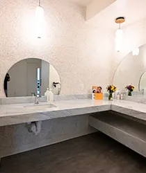 Modern bathroom vanity with round mirror, long countertop, sink, and flowers under pendant lights.