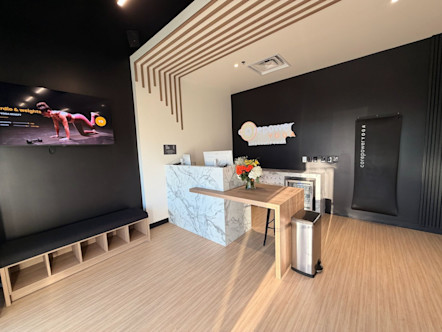 Modern yoga studio reception with marble desk, wooden accents, and fitness display screen showing workout demonstration