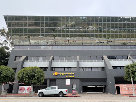 Yellow CorePower Yoga sign out front of a large dark grey stucco building with the upper half of the building having reflective exterior windows