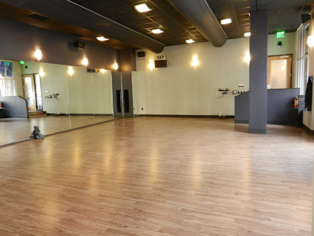 Naturally lit yoga studio space with warm wooden floors and a mirrored, cream wall with gray ceilings