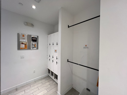 La Cañada CPY locker room with white walls, while tiled floors, double row of coat racks, and a unit of white lockers with cubby spaces below