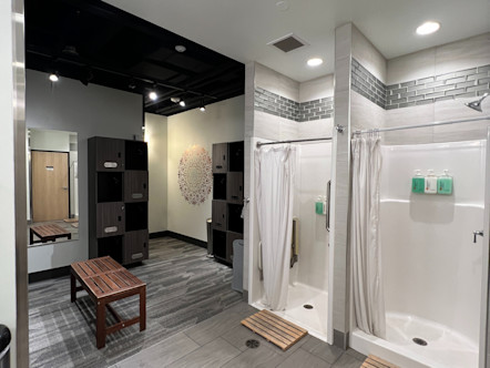 CorePower Yoga locker room area with two showers side by side and a multishaded, grey carpet with brown lockers to the side