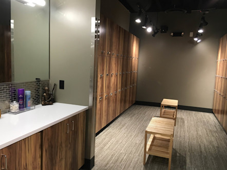 Warm wooden lockers surrounding two tan wooden benches near a vanity and large mirrors