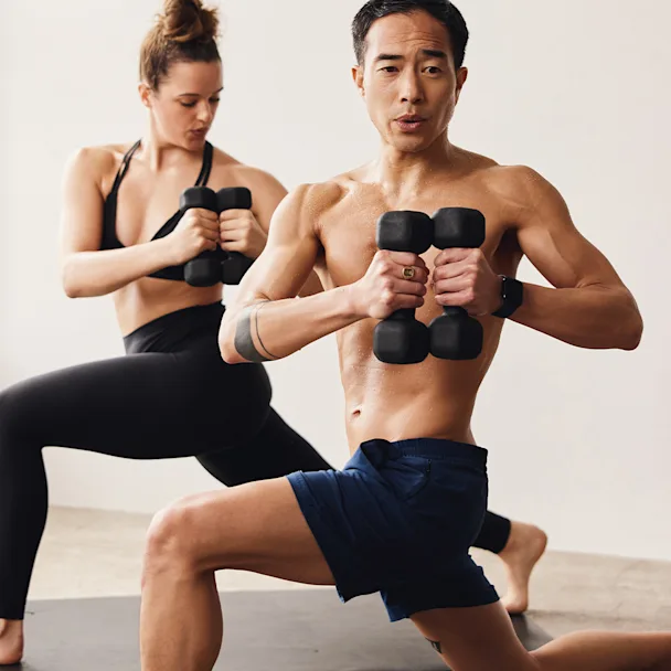 Two yogis in a twisted lunge position each holding black dumbbells close to their chests