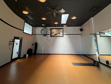 CPY studio room with light tan wooden floors, canvas colored walls with black trim, and a black paneled ceiling