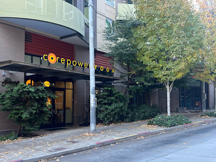 Orange CorePower Yoga sign underneath a light green balcony with greenery on either side of the windowed studio entrance