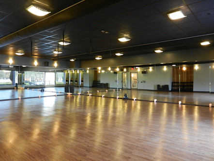 Yoga studio space with warm wooden floors with mirrored walls and overhead lighting