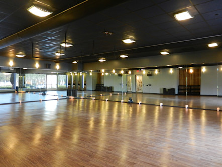 Yoga studio space with warm wooden floors with mirrored walls and overhead lighting