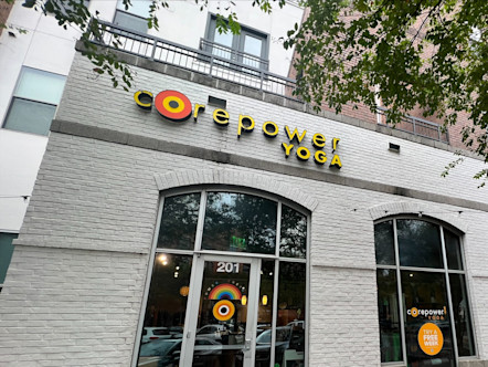CorePower Austin Triangle studio's exterior white brick wall with the orange logo touted above glass doors
