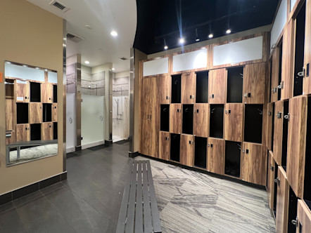 Brown wooden lockers and cubbies with a grey bench in front on top of split flooring with dark grey tile and grey patterned carpet