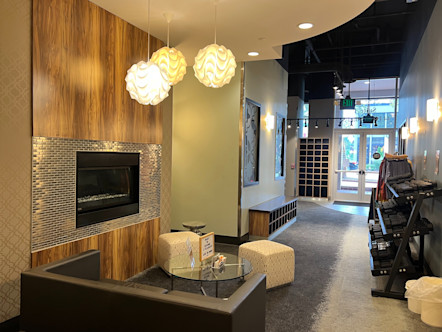 Front lobby area with a metal tiled and wooden paneled fireplace next to a seating area with a brown couch and glass table 