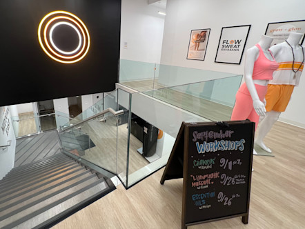 Black wall with neon CPY logo directly adjacent to white walled hallway with three picture frames holding three CPY posters