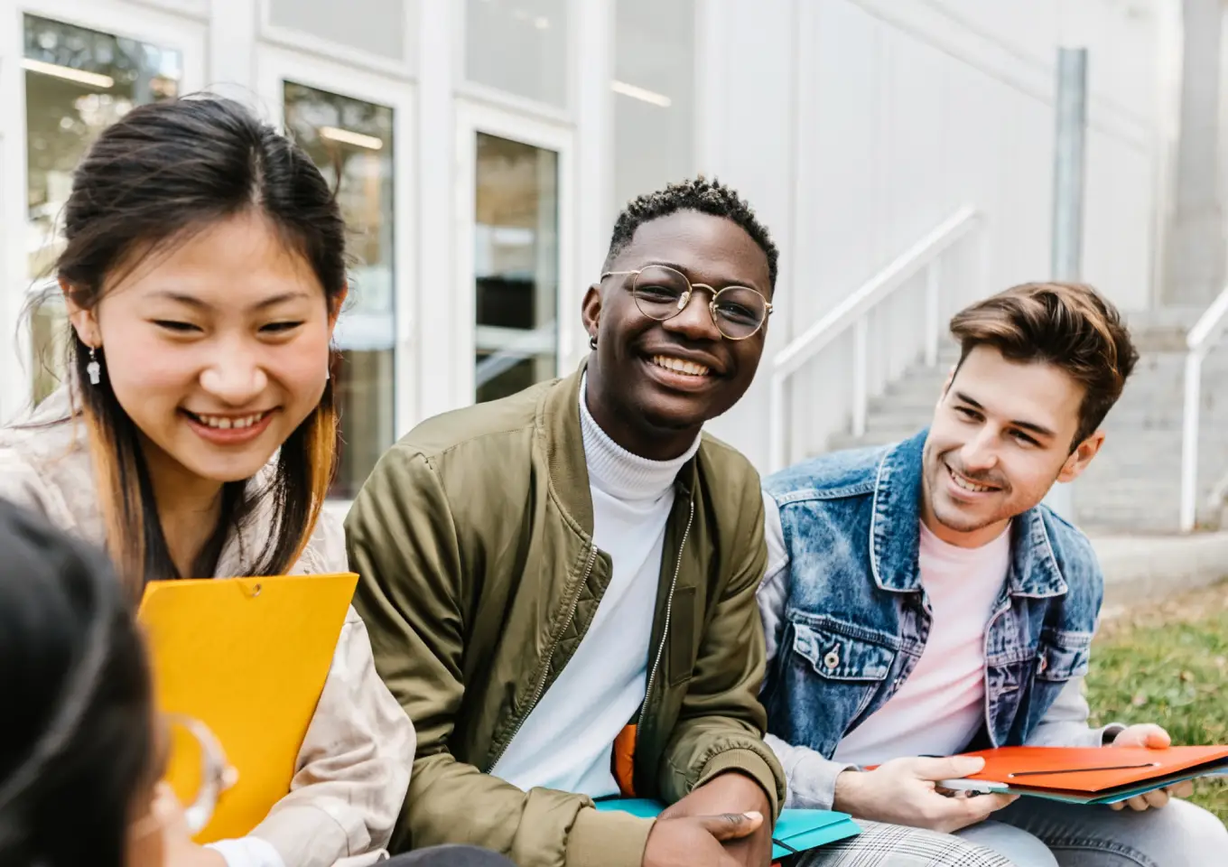 Three students sitting and smiling outdoors.