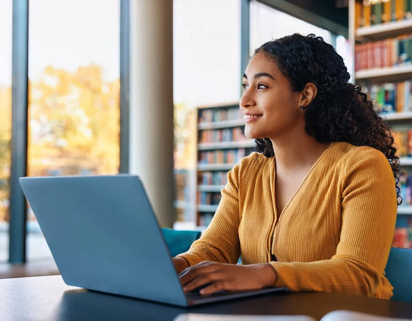 A photograph of a female student at a university studying in a library looks thoughtfully in