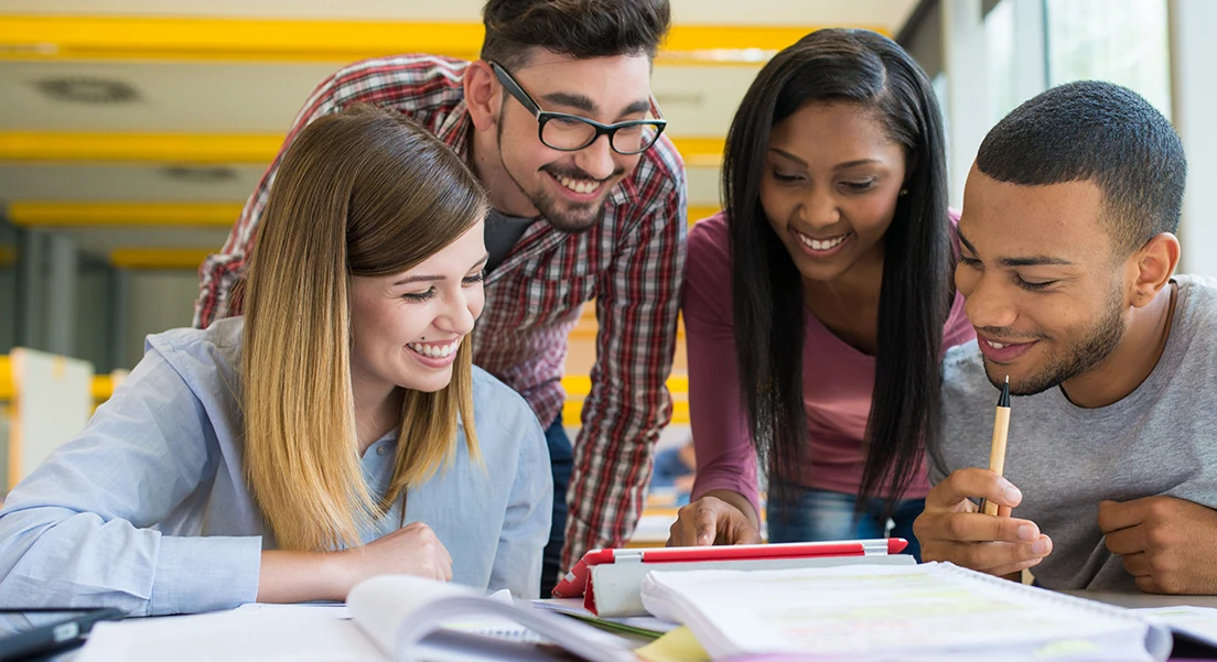 Students gathered around a laptop, smiling