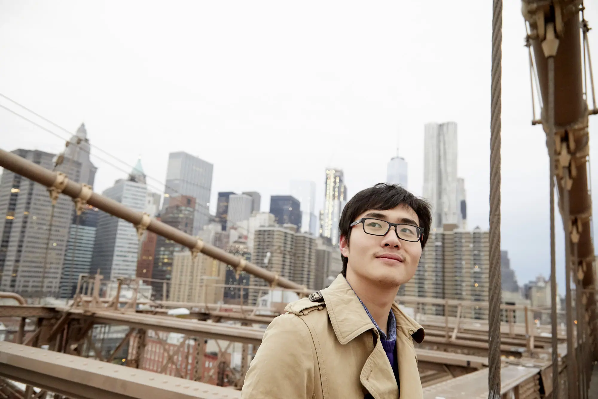 man in trench coat leaning against bridge outdoors