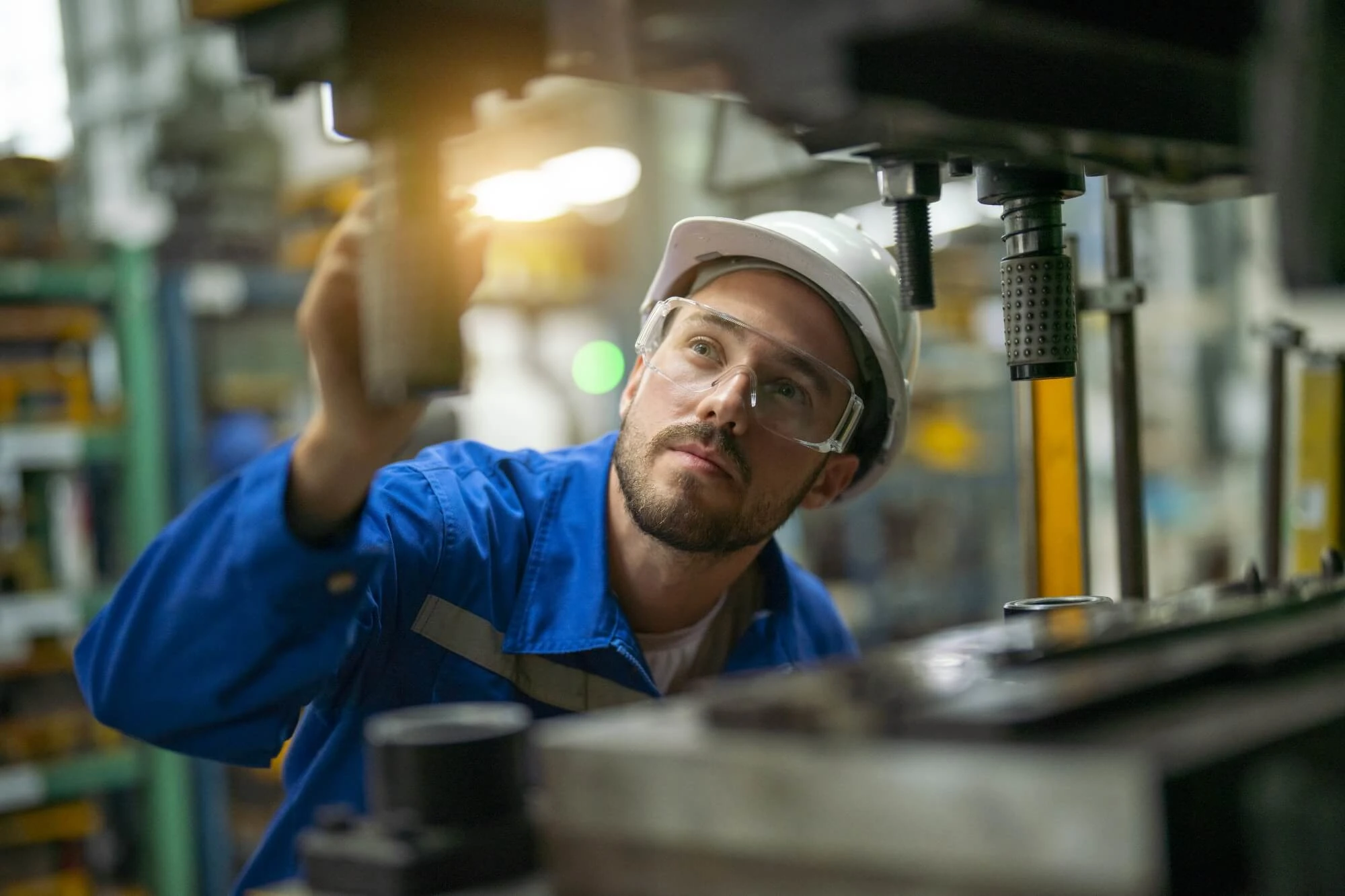 man in a factory setting wearing hard hat and safety glasses