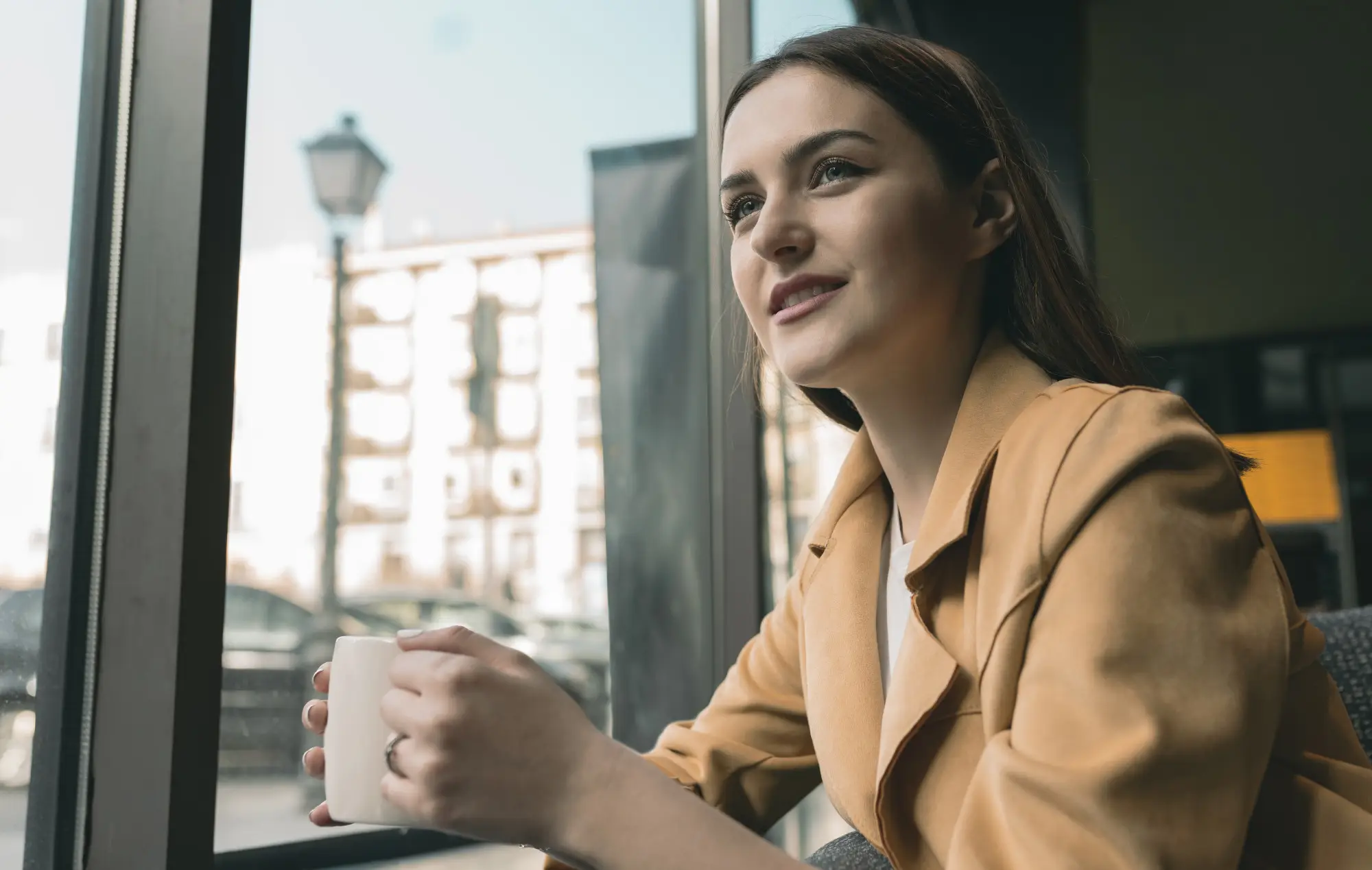 woman with suit jacket holding a mug sitting by a window