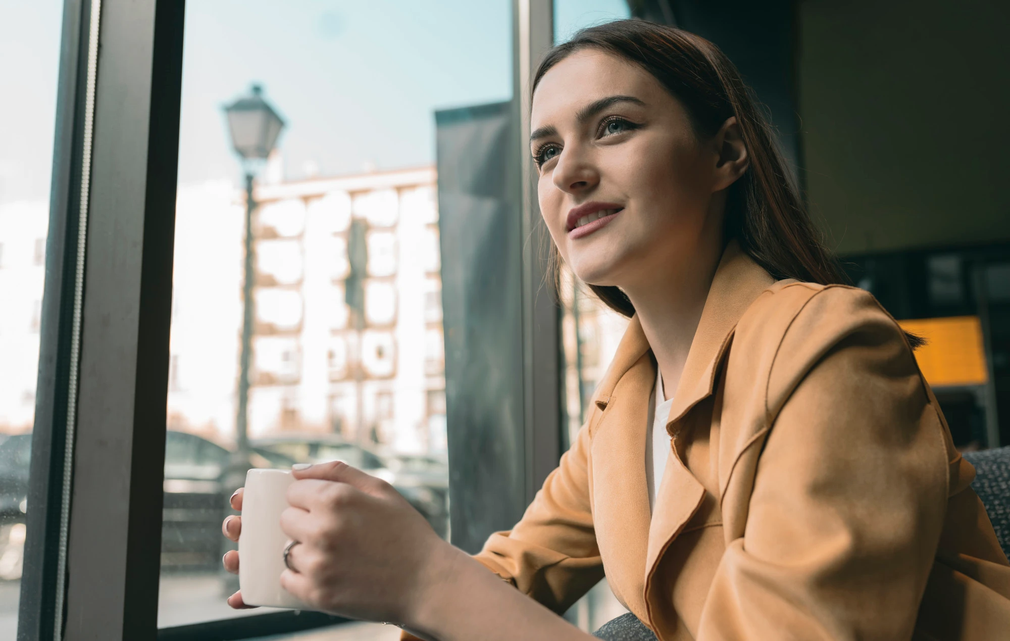 woman with suit jacket holding a mug sitting by a window