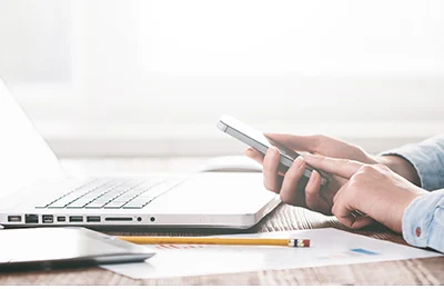 person-studying-for-the-cfa-exam-using-a-smartphone-alongside-a-laptop-and-study-materials-on-a-desk