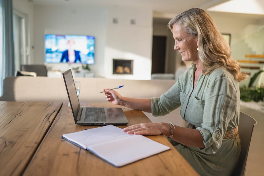 Smiling female real estate instructor working on a laptop at home, seated at a table.