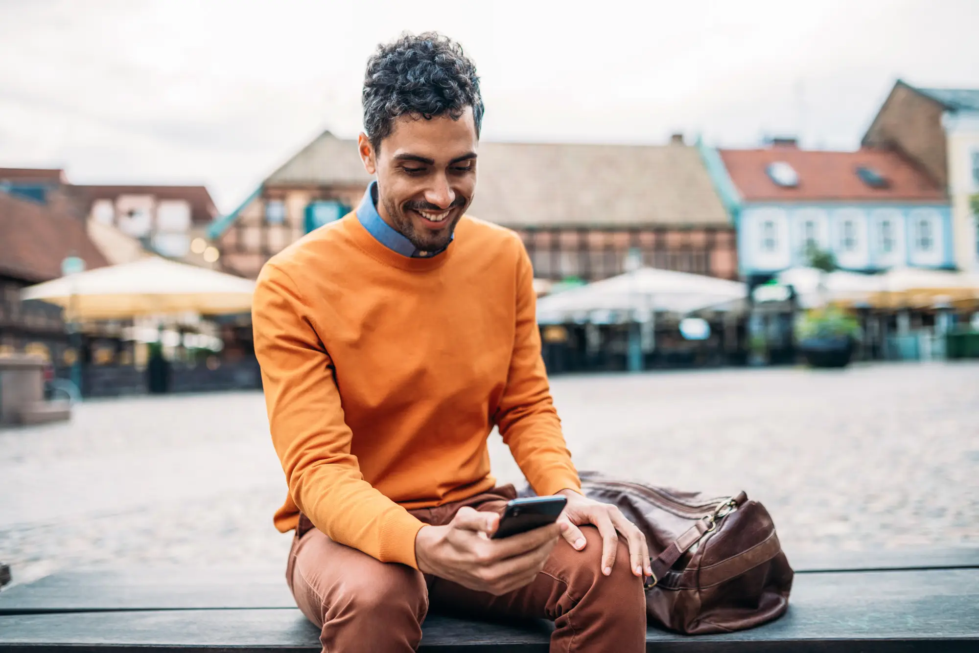 man outdoors by the water sitting on the bench with hone in hand