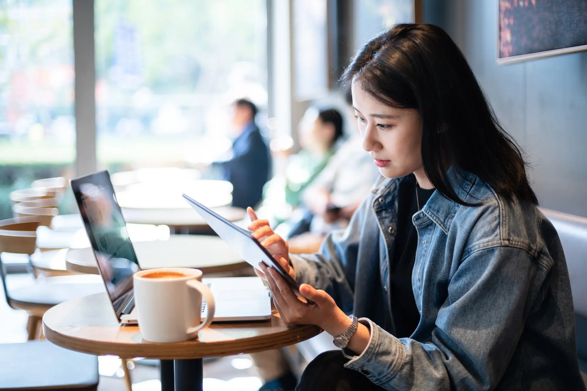 一位女士坐在咖啡店里，手里拿着平板电脑