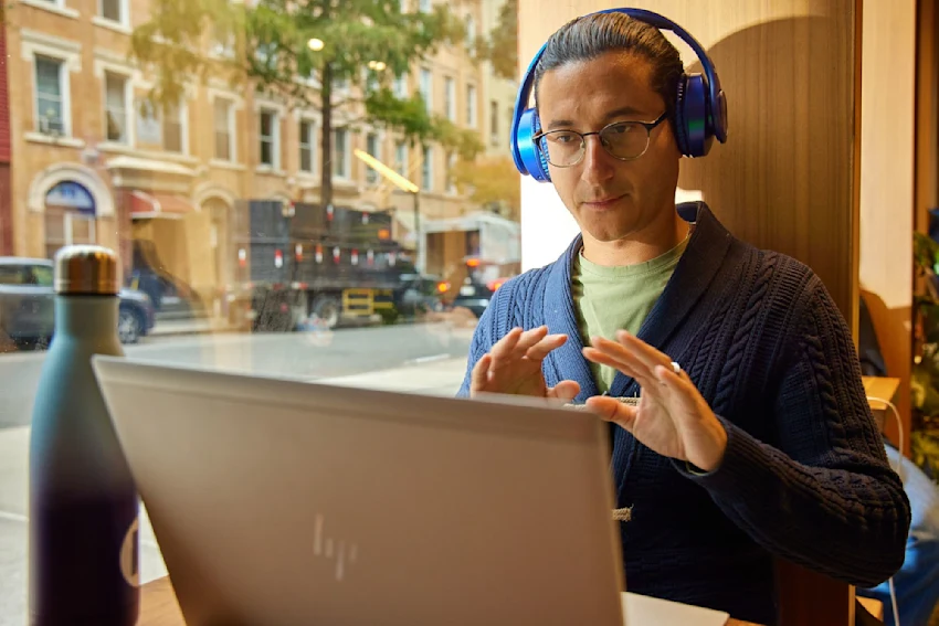 Our Kaplan Culture - Changing Education - man in cafe with laptop and headphones in virtual meeting
