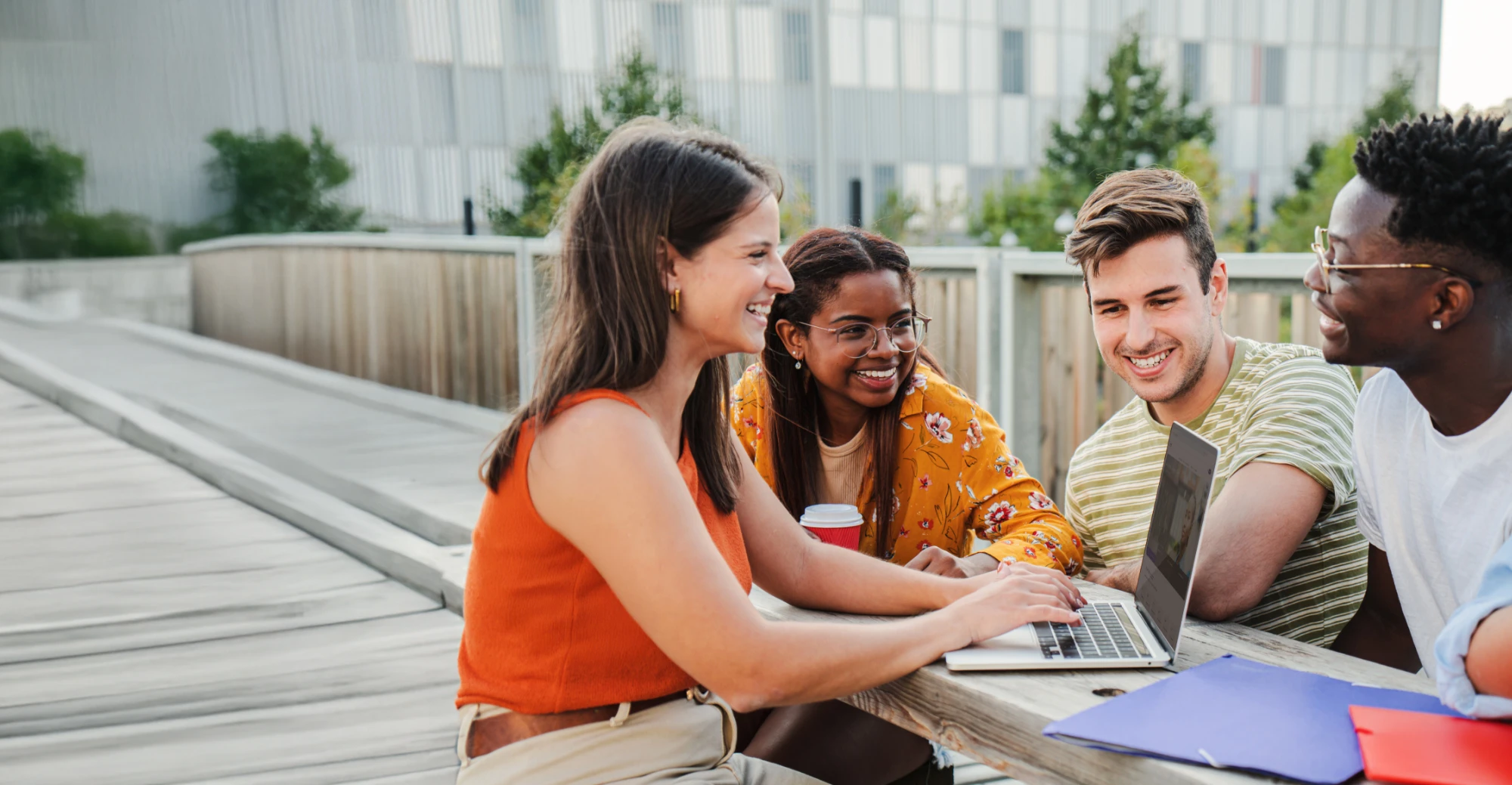Four smiling students, sitting at a table outside on a school campus