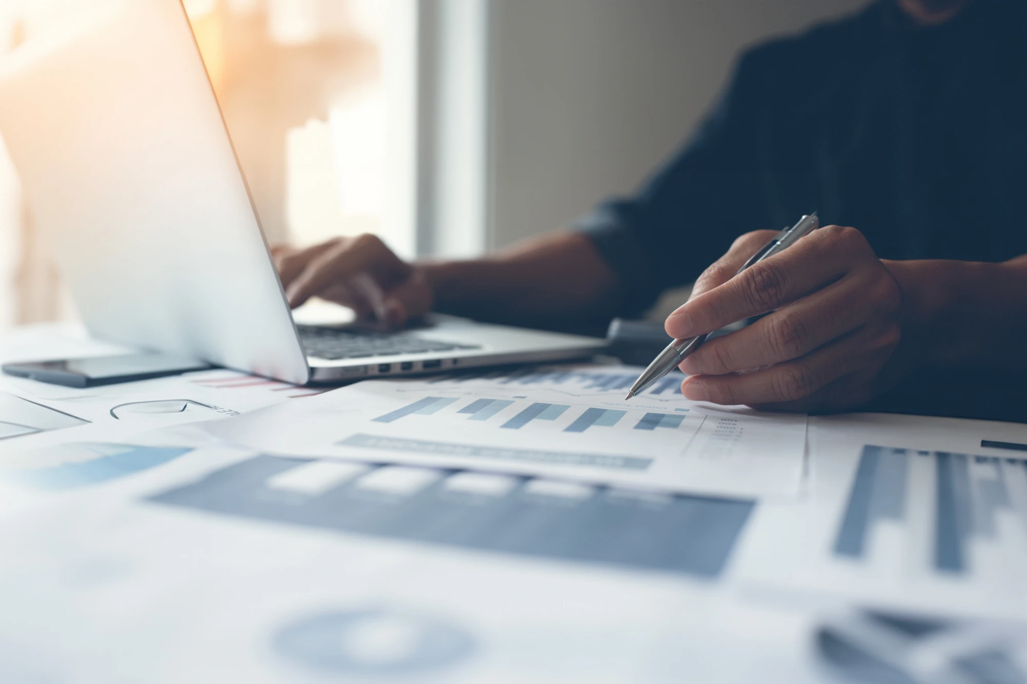 person working on laptop charts on paper