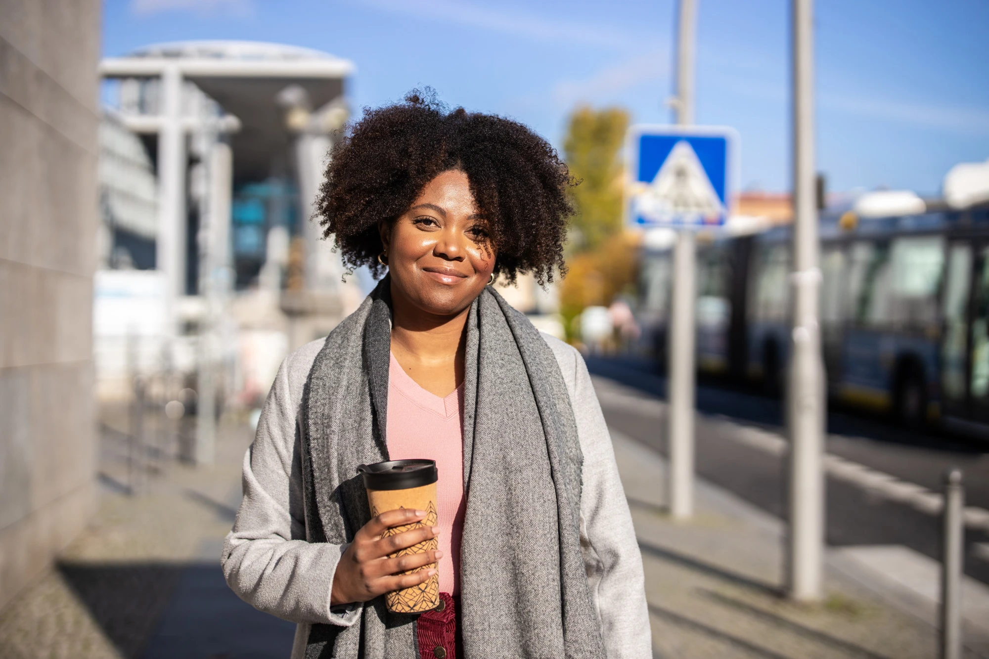 Smiling woman with a coffee cup in hand standing outdoors