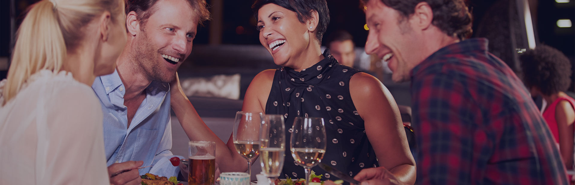 Eine Gruppe von Freunden sitzt an einem Tisch, sie essen zu Abend, trinken Wein und sprechen über festen Zahnersatz.