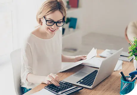 Eine etwa 30-jährige Frau mit Brille sieht in ihrem Laptop nach, wie viel Zahnersatz kostet. Sie lächelt, denn sie hat Vertrauen in blend-a-dent, egal wie sie sich entscheidet. 