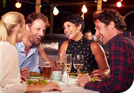 Eine Gruppe von Freunden sitzt an einem Tisch, sie essen zu Abend, trinken Wein und sprechen über festen Zahnersatz.