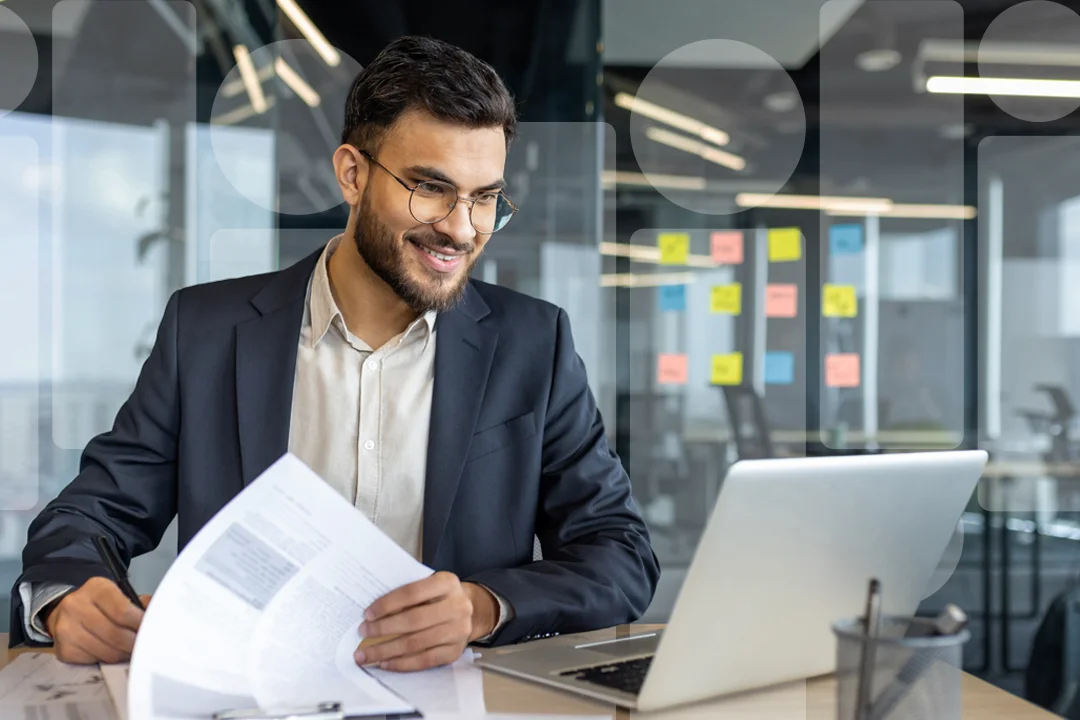 A man with paperwork looking at a laptop