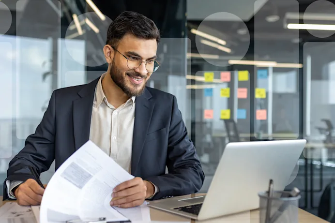 A man with paperwork looking at a laptop