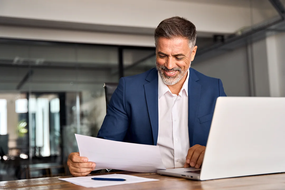 Man looking at a laptop holding paperwork