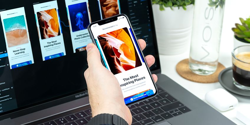 App open on phone with designs open on a computer screen behind