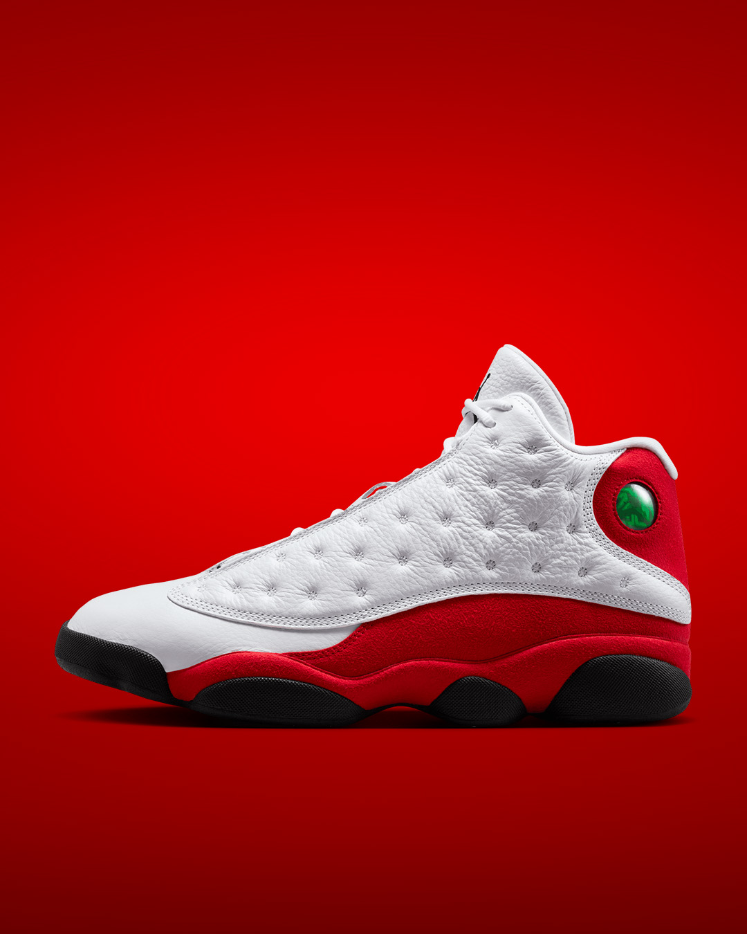Air Jordan 13 Retro White True Red men's basketball shoe featuring premium quilted white leather upper, vibrant red suede overlays, iconic green hologram eye detail and black rubber outsole. Classic Jordan Brand sneakers inspired by Michael Jordan's legacy, now available at KICKZ.