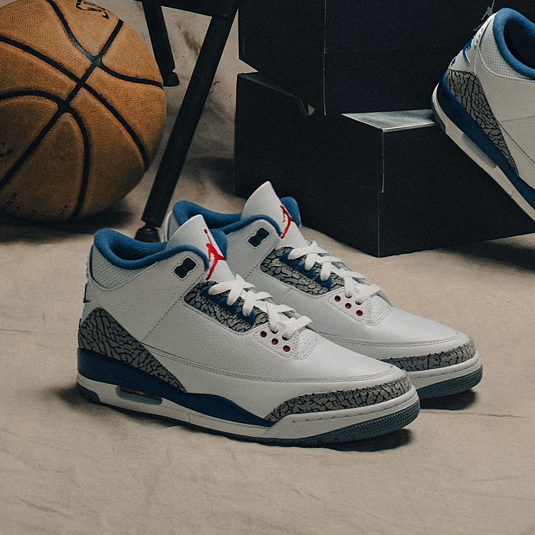 Front angle view of Air Jordan 3 Retro OG 'True Blue' sneakers with elephant print detailing and blue heel accents, styled with a basketball and additional pair in the background