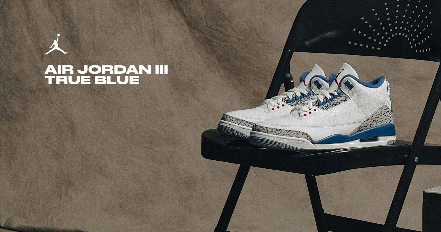 Air Jordan 3 Retro OG 'True Blue' basketball sneakers in white, cement grey and true blue, displayed on a black folding chair with the Jumpman logo and 'Air Jordan III True Blue' text in the background
