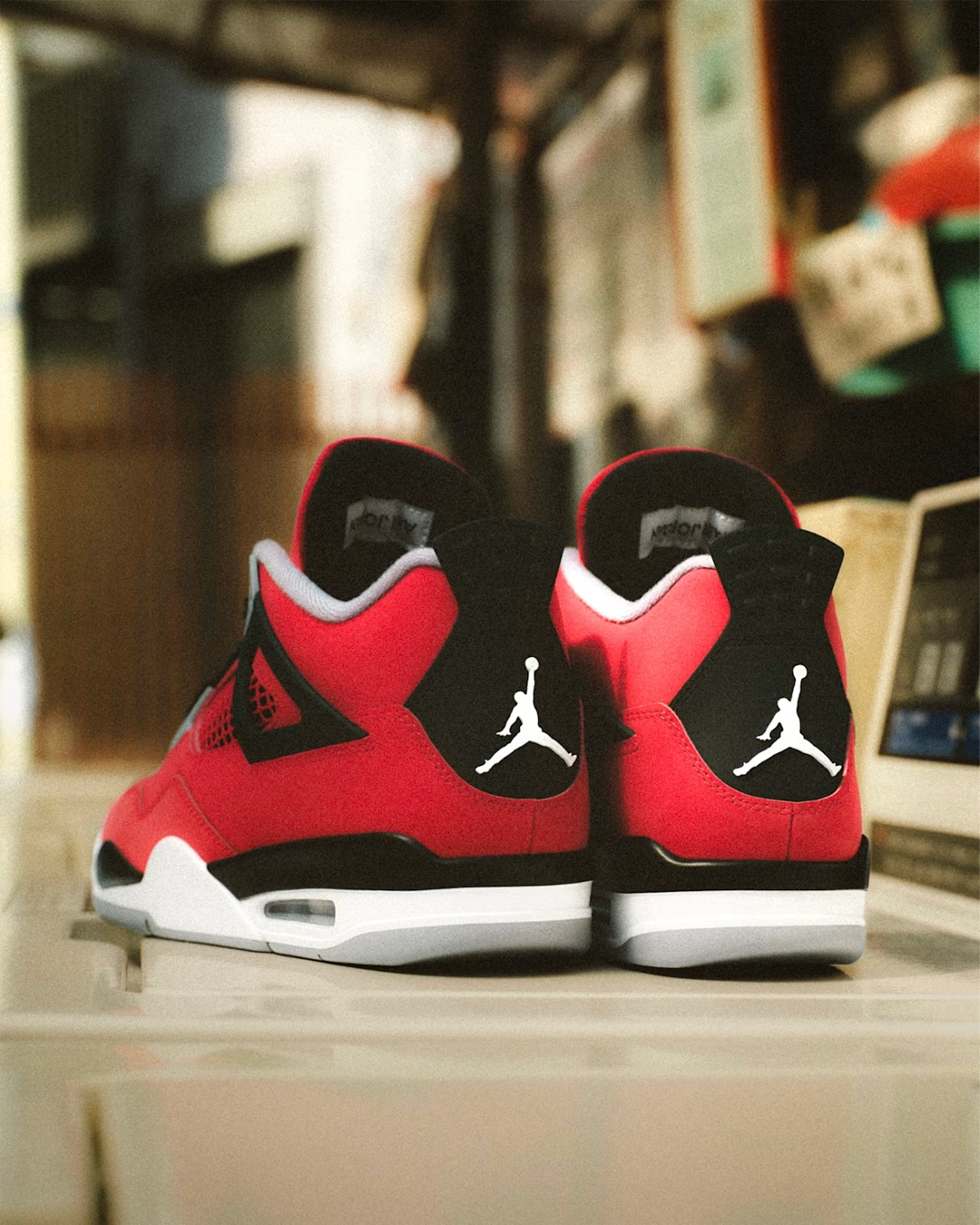 Back view of Air Jordan 4 Retro 'Toro Bravo' sneakers displaying Fire Red nubuk upper, black heel tabs with white Jumpman logos, and white Air cushioned midsole on wooden surface